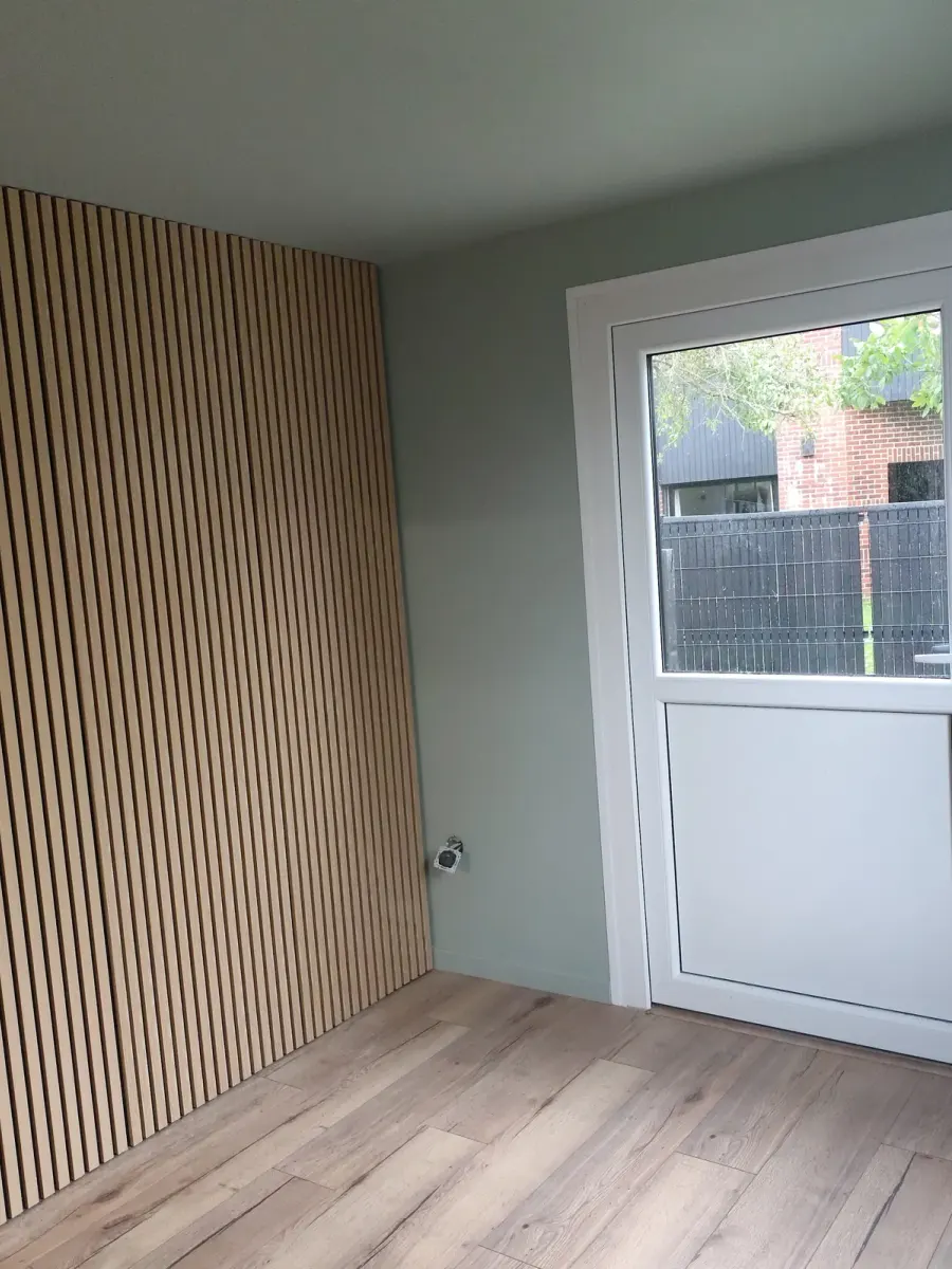 Bureau après travaux : mur habillé de tasseaux de bois, murs gris-vert clair, sol stratifié chêne