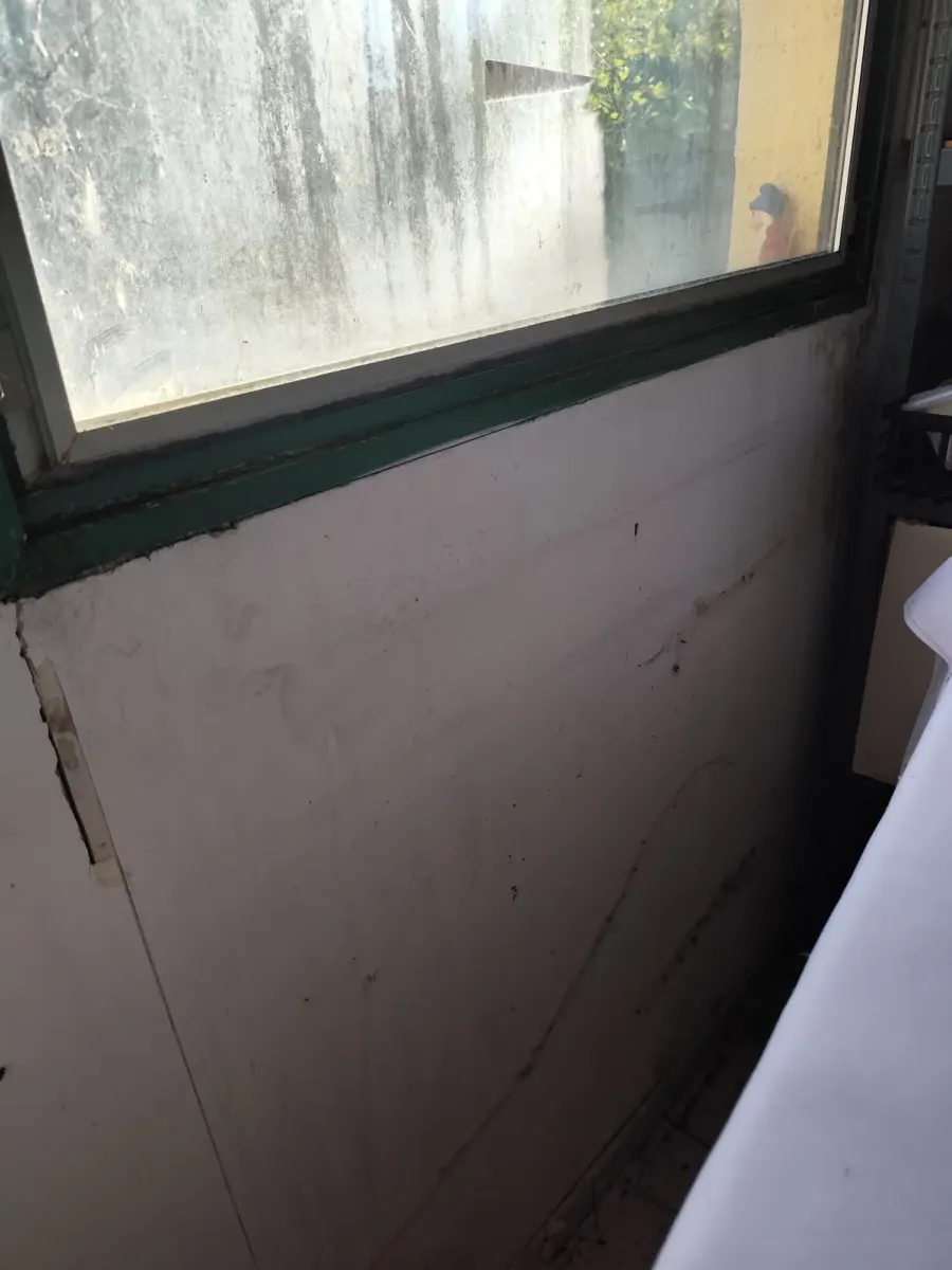 Local de réserve avant travaux : sous la fenêtre à l’encadrement vert, mur en plaques de plâtre abîmé et taché