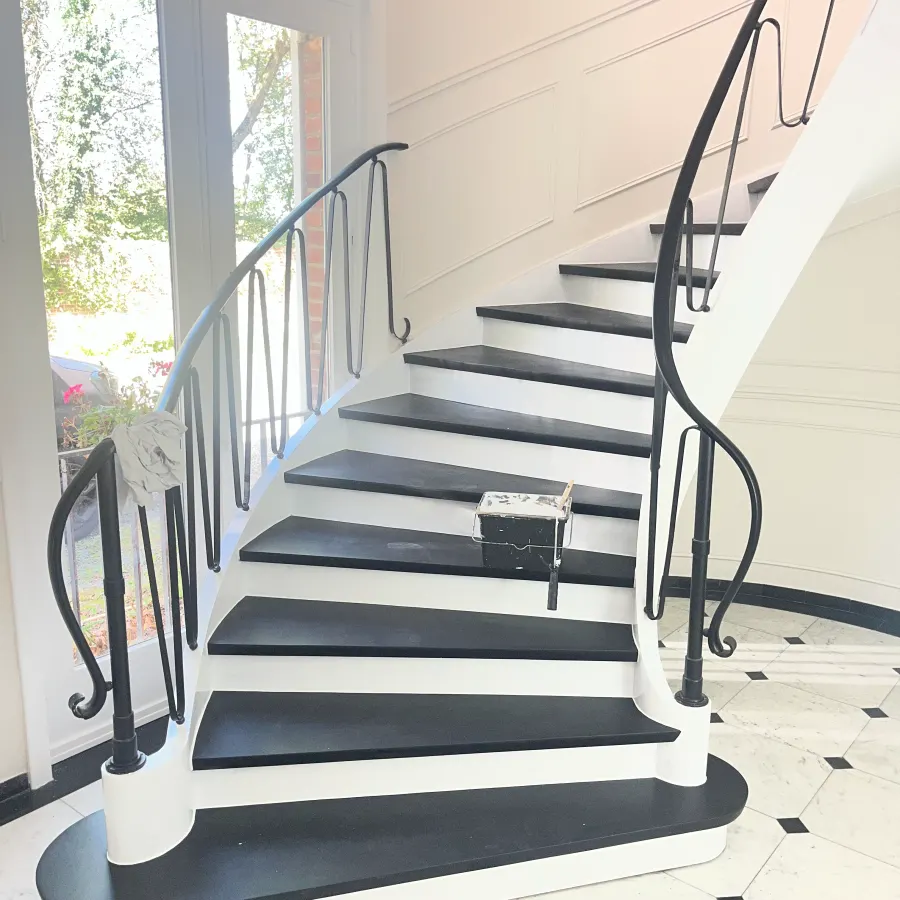 Escalier aux marches noires et contremarches blanches, rampe en fer forgé conservée