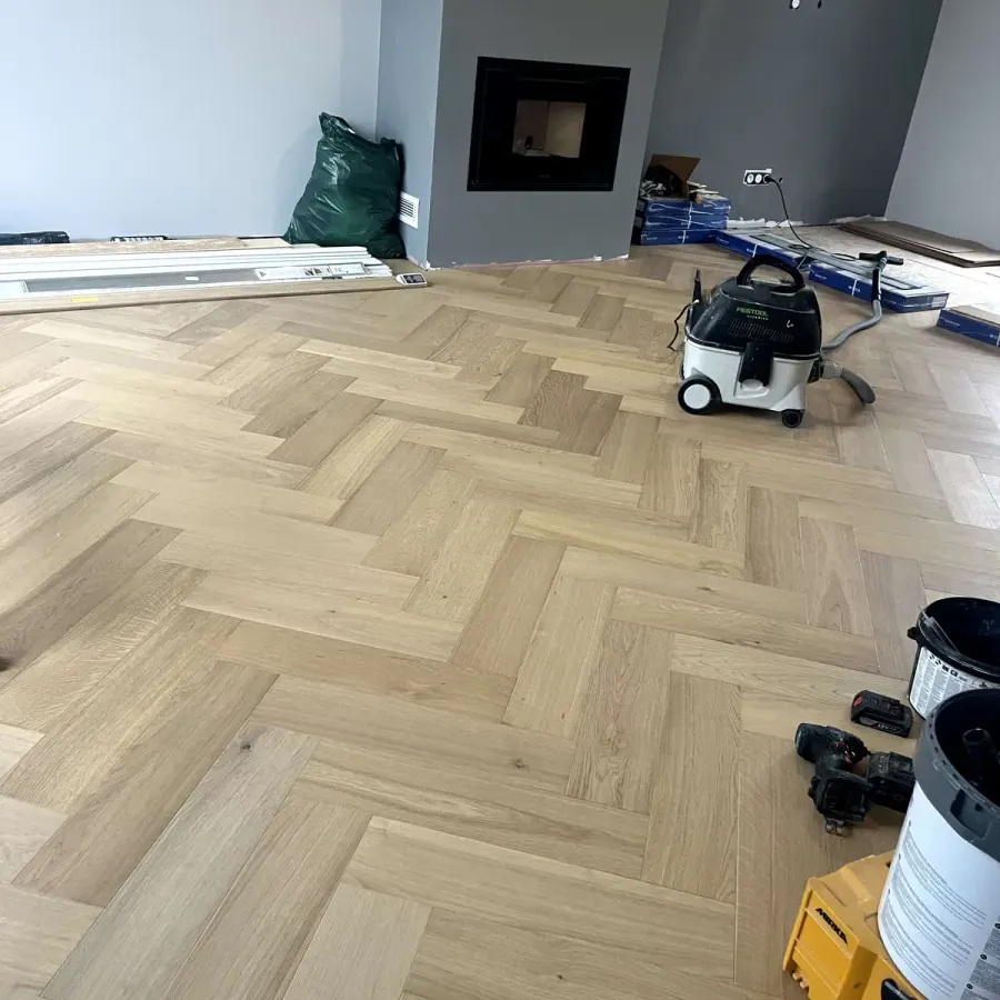 Parquet en chevron chêne clair fraîchement posé, mur gris au fond