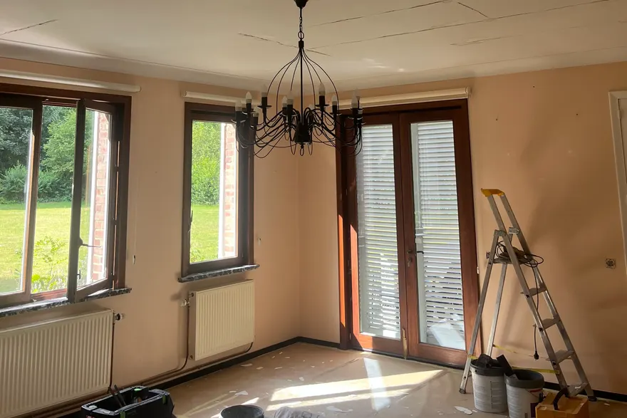 Grande pièce au début du chantier : plafond fissuré, murs beiges, menuiseries en bois foncé, lustre en fer forgé