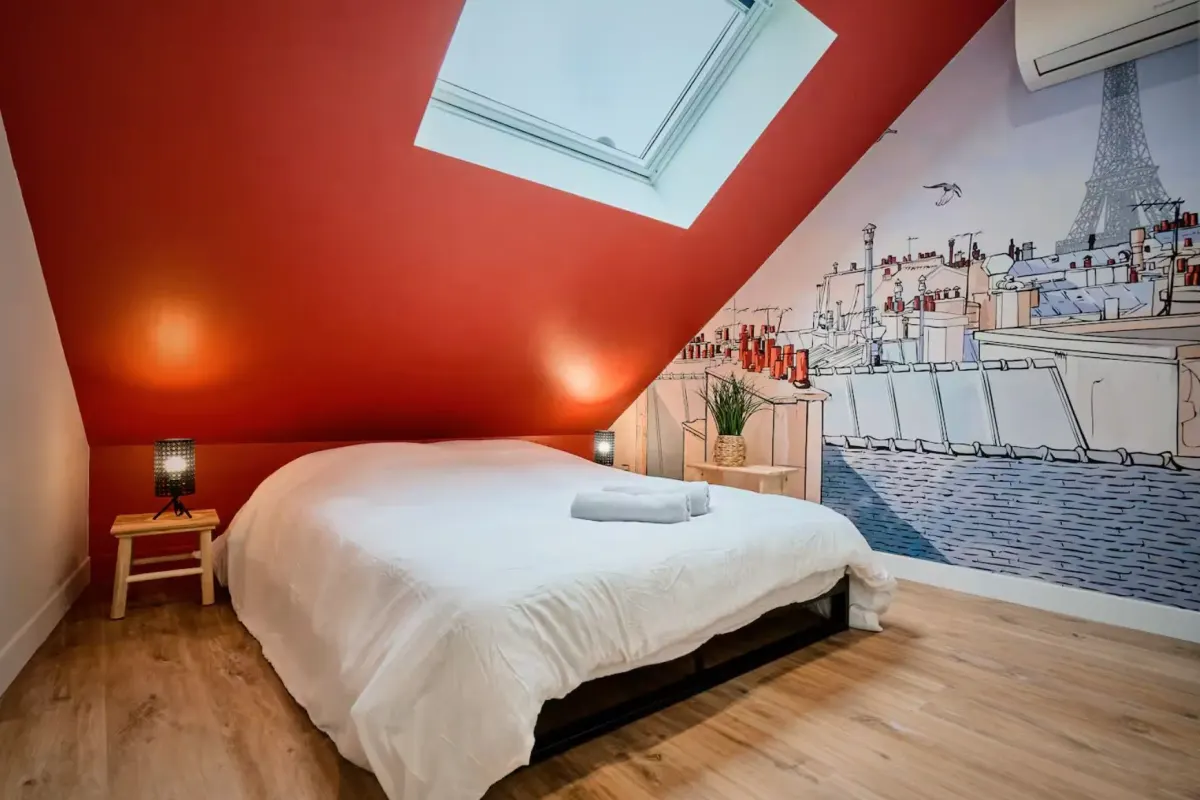 Chambre sous rampant au mur et à la pente de toit peints en rouge terracotta, avec fresque murale sur le pignon