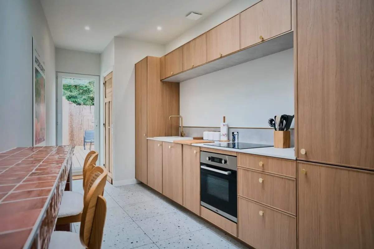 Cuisine aux façades de bois clair, murs et plafond blancs, sol en terrazzo