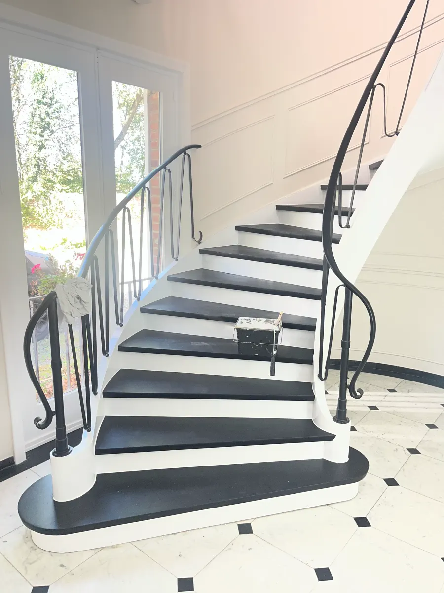 Cage d'escalier rénovée : marches noires, contremarches blanches, rampe en fer forgé et soubassement mouluré