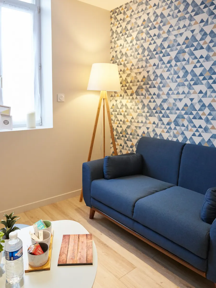 Pan de mur habillé d’un papier peint à triangles bleus et dorés, lampadaire et canapé bleu