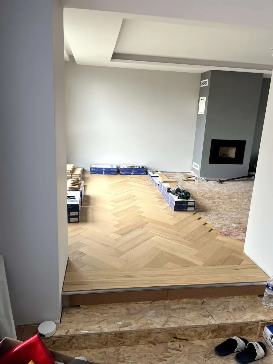 Pose du parquet en chevron chêne clair en cours, sur un plancher en panneaux de bois