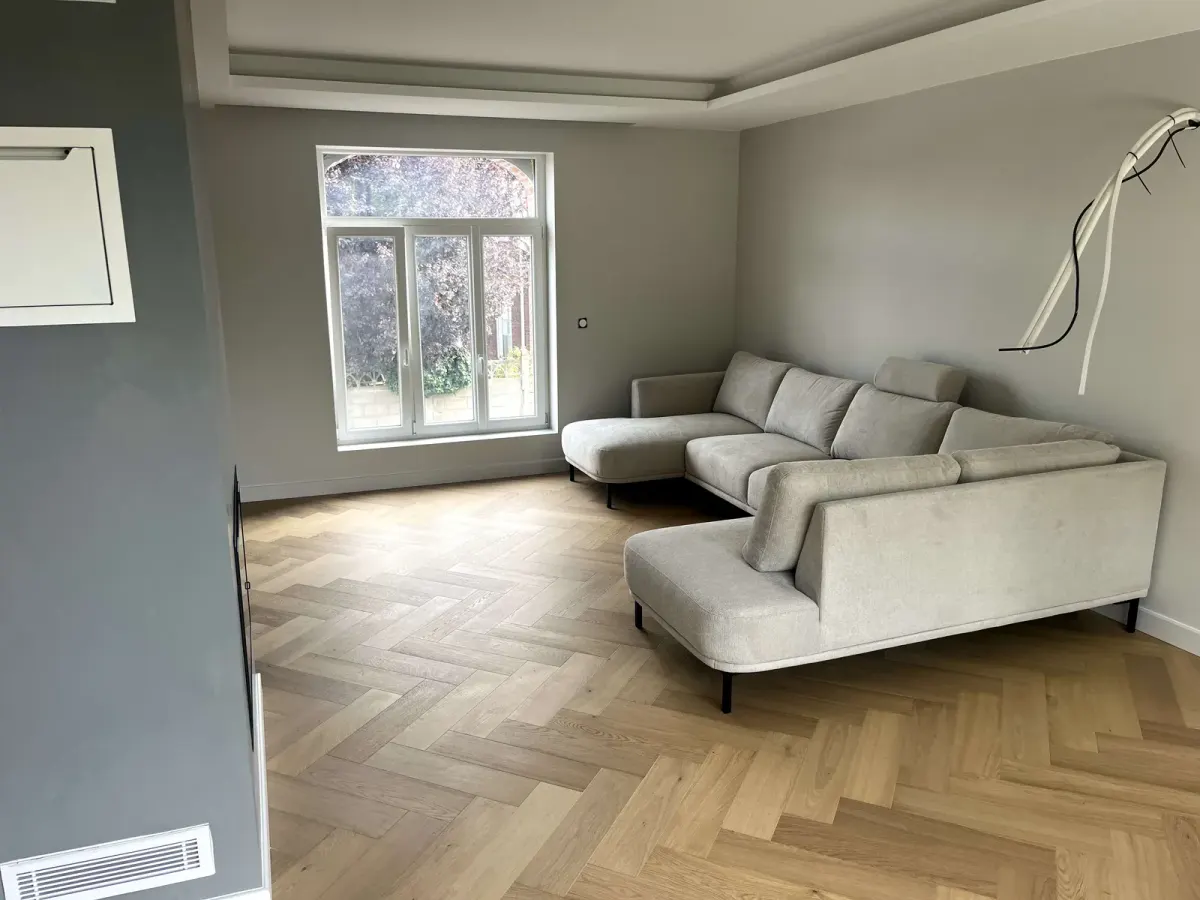 Salon au parquet en chevron chêne clair, murs gris clair et grand canapé d'angle