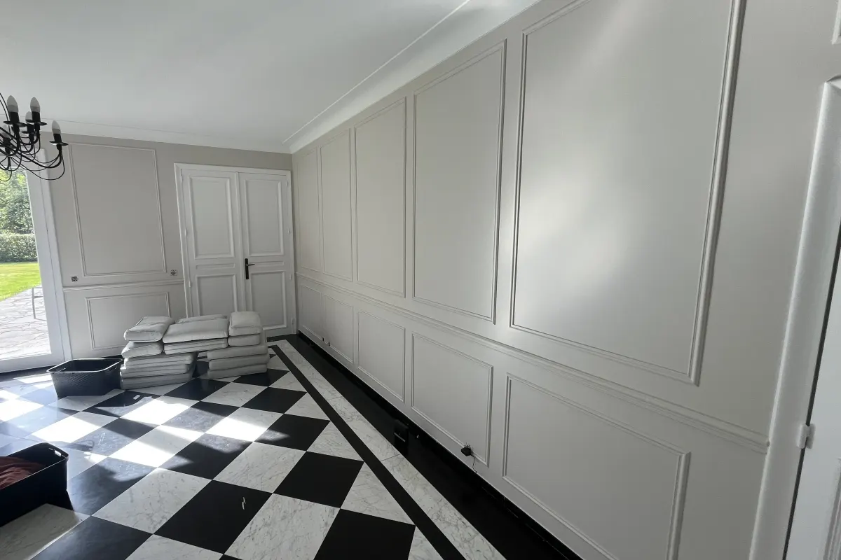 Pièce dont les murs à panneaux moulurés viennent d’être peints en blanc, sol en damier noir et blanc