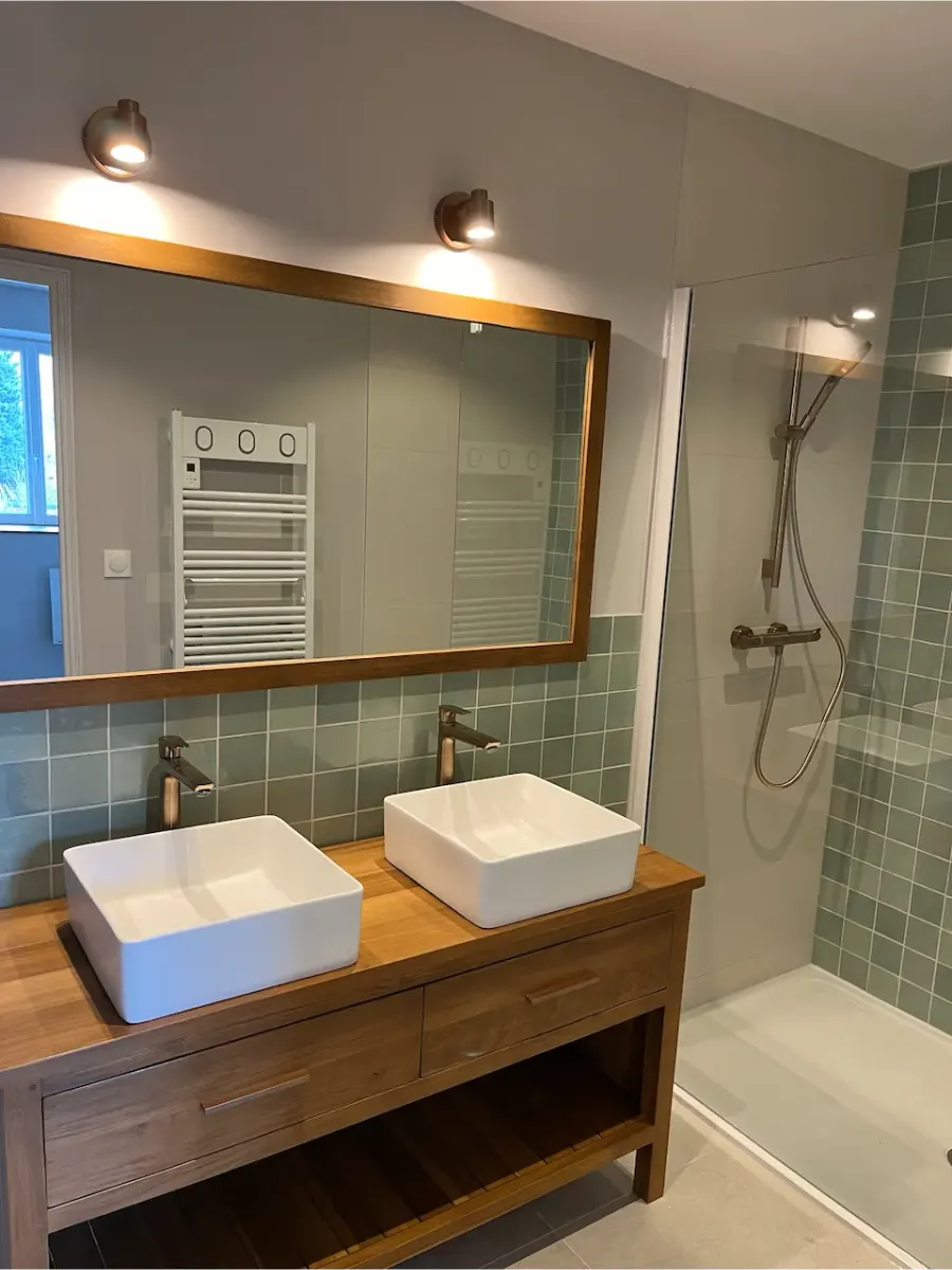 Salle de bain aux murs repris en gris clair au-dessus d’une faïence vert d’eau, double vasque sur meuble en bois