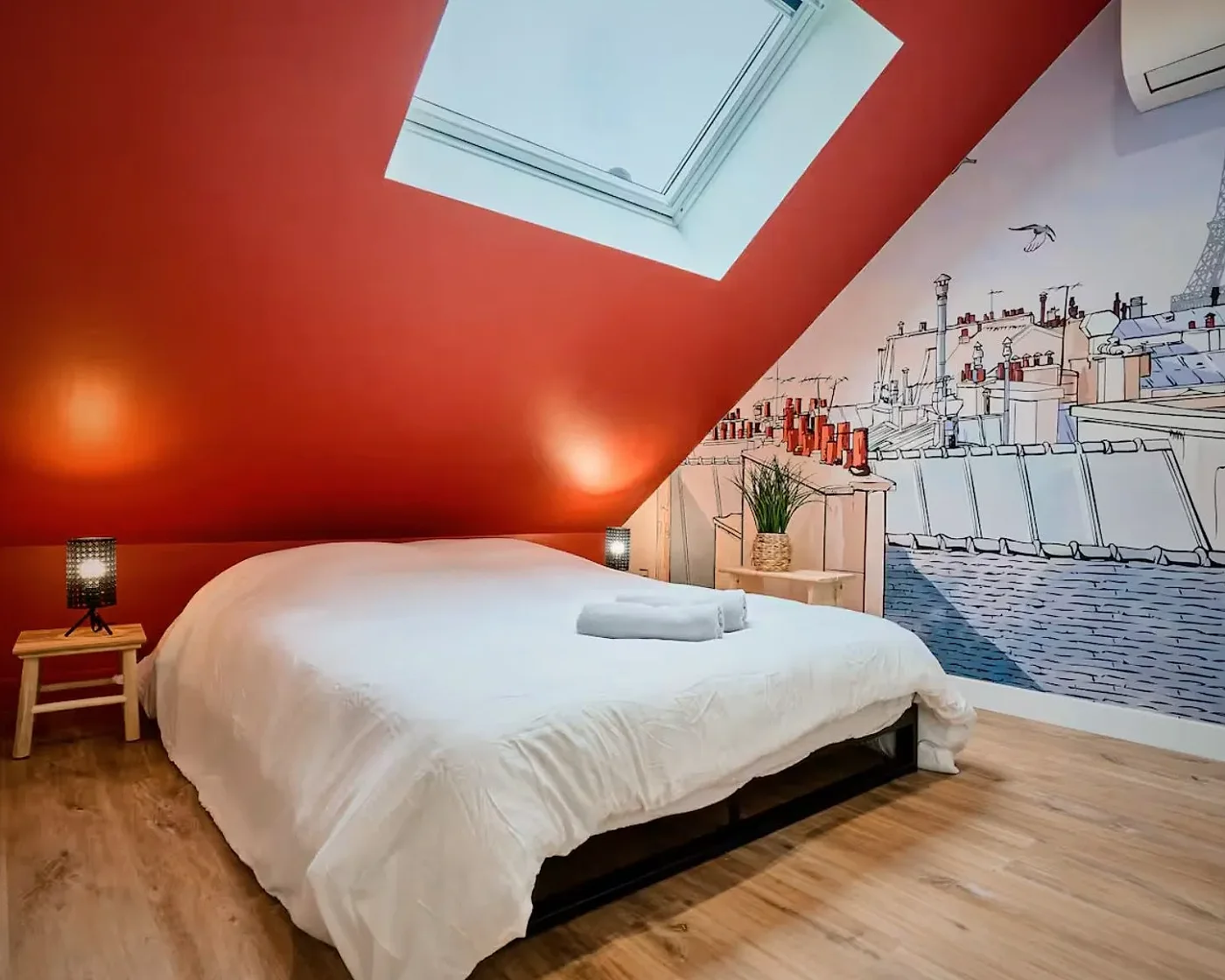 Chambre sous rampant au mur et à la pente de toit peints en rouge terracotta, avec fresque murale sur le pignon