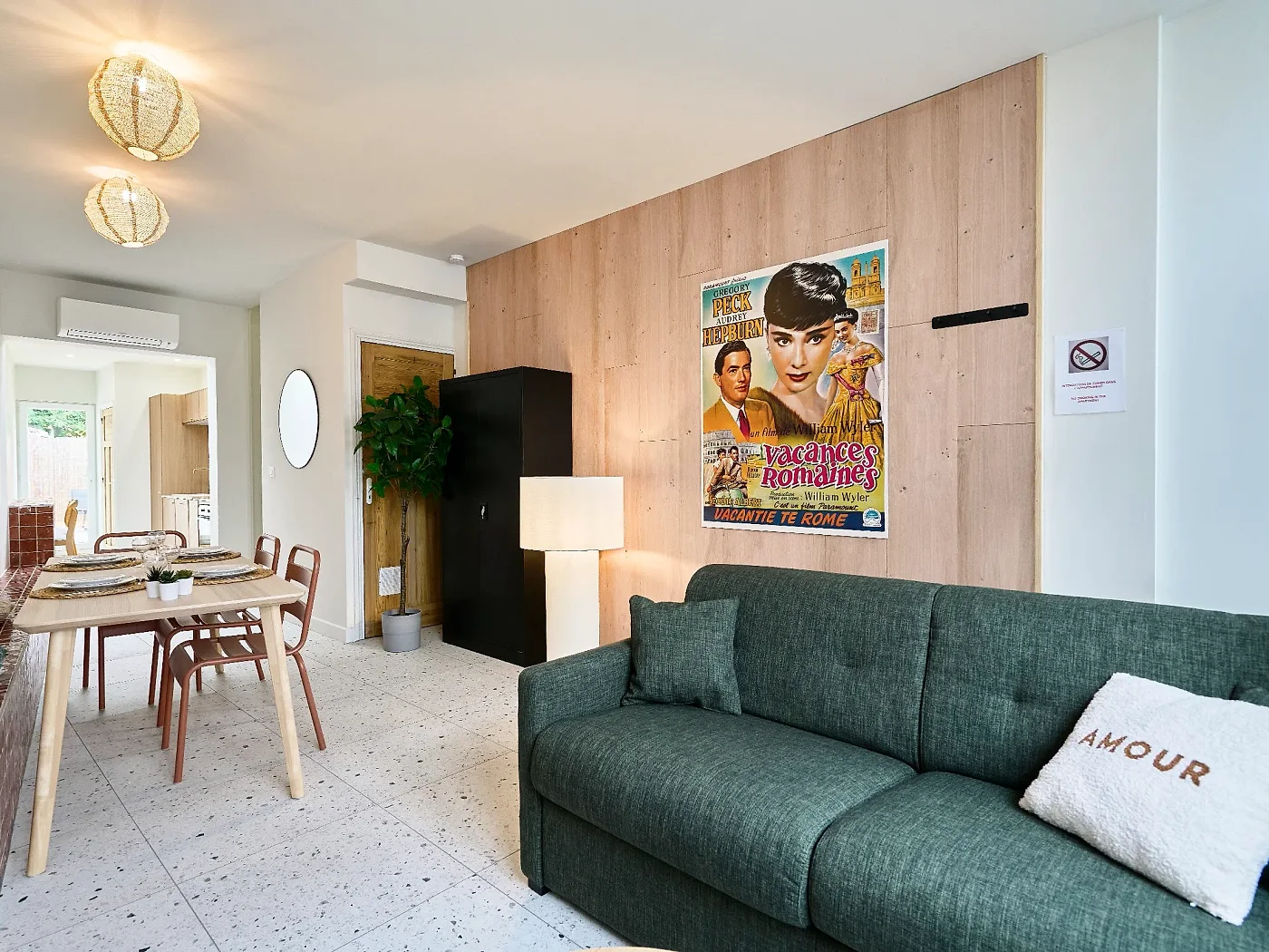 Séjour aménagé : mur habillé de bois clair, canapé vert, table à manger et sol terrazzo