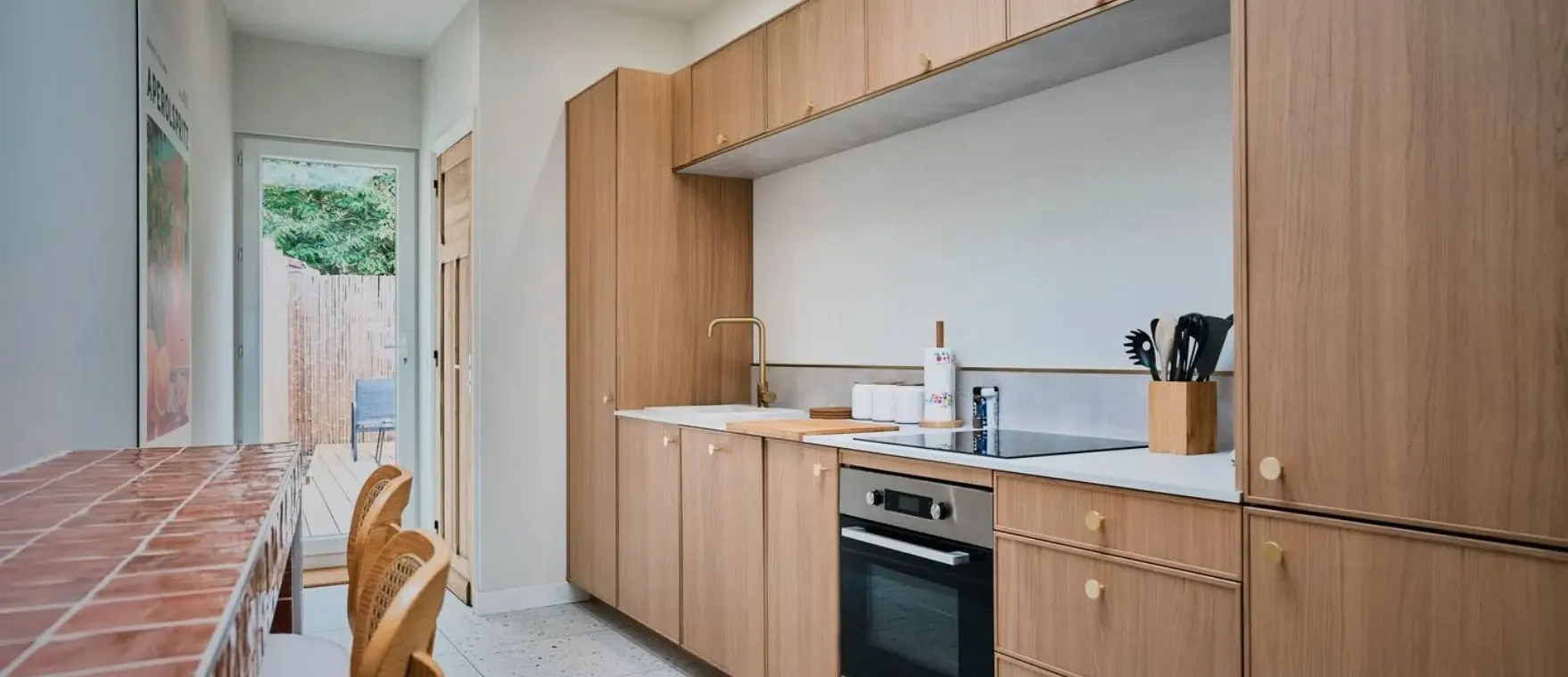 Cuisine aux façades de bois clair, plan de travail blanc et sol en terrazzo