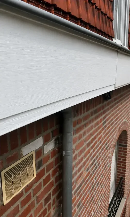 Le même bandeau de rive repeint en blanc, surface lisse, au-dessus du mur de brique